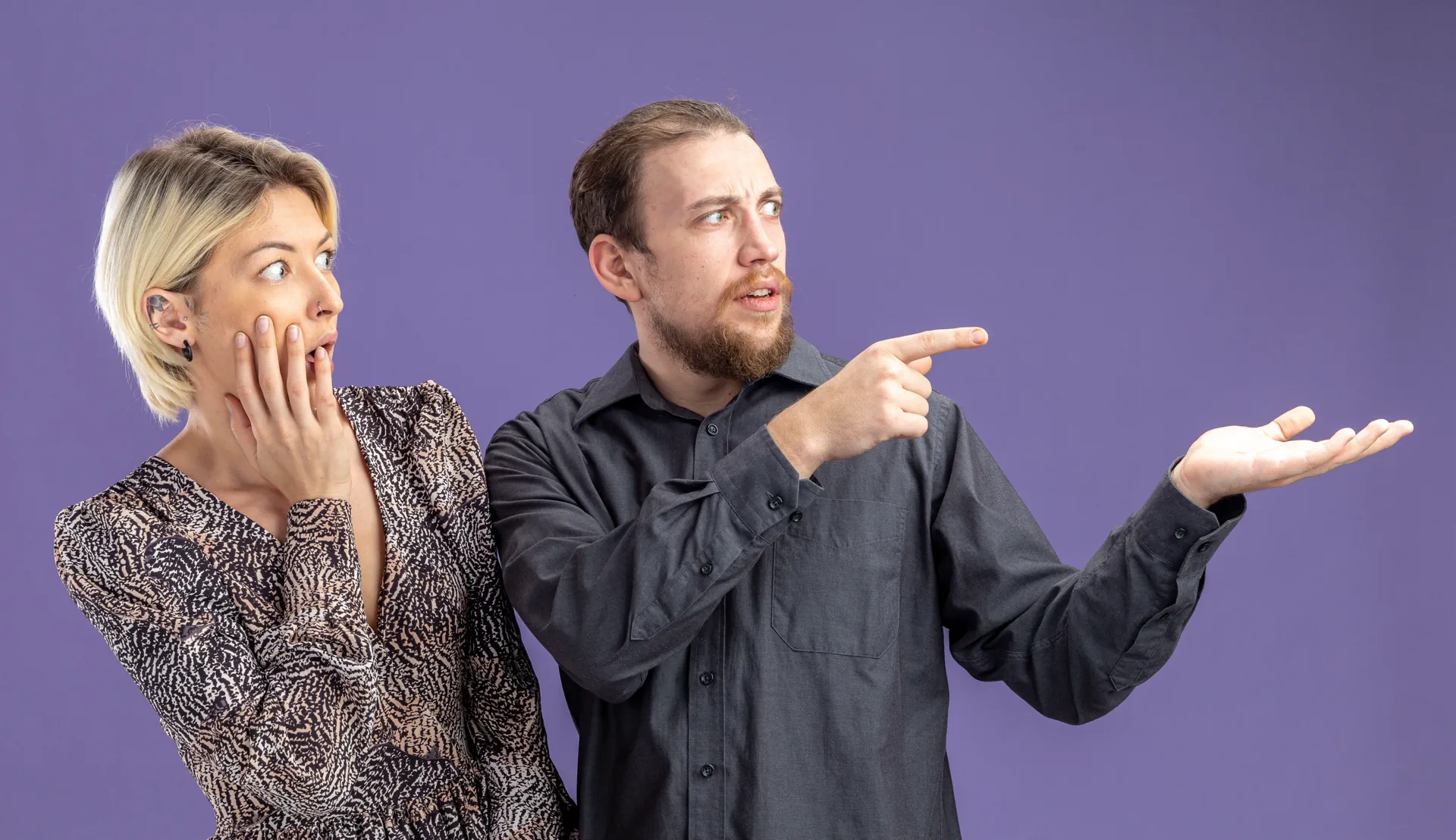 young beautiful couplesurprised man woman looking aside pointing with index fingers theside valentines day concept standing purple wall